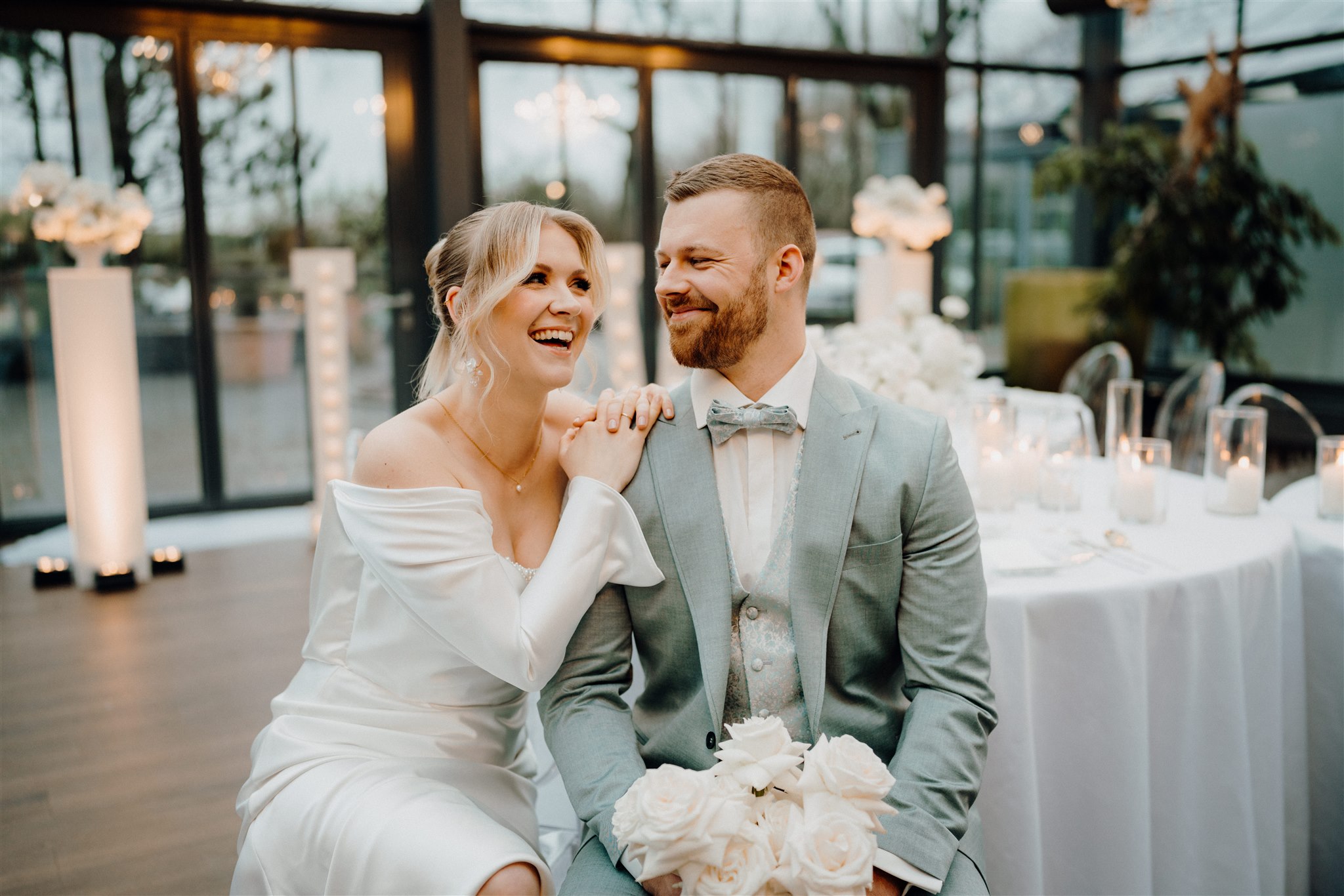 Braut und Bräutigam sitzen vor ihrem Tischsetup und lachen zusammen, Planung: von Aspern Weddings