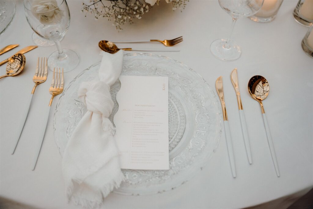 Tischdekoration auf einem runden Tisch mit Glastellern, Leinenservietten und goldenem Besteck, Dekoration: Atelier Feingefühl, Planung: Von Aspern Weddings