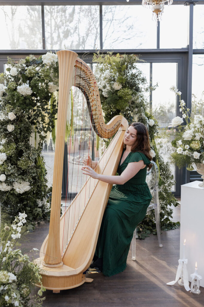 Harfinistin spielt auf der Harfe vor dem Traubogen mit opulenten Blumen, Planung: Sophia von Aspern, von Aspern Weddings, Lüneburg, Hamburg, Hannover, Bremen