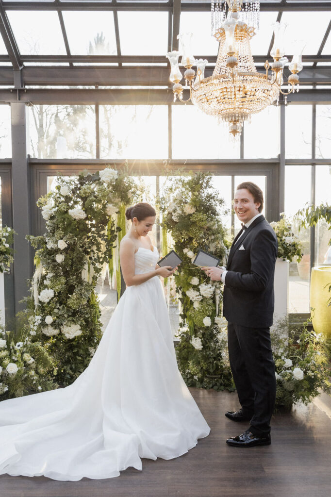 Braut und Bräutigam stehen vor dem Traubogen, über ihnen hängt ein funkelnder Kronleuchter. Die florale Dekoration und das Licht des Kronleuchters verleihen der Szene eine luxuriöse, festliche Atmosphäre. Dieser Moment spiegelt den exklusiven Stil von Hochzeiten wider, die durch Sophia von Aspern mit von Aspern Weddings in Hamburg, Bremen, Hannover und Niedersachsen geplant werden.