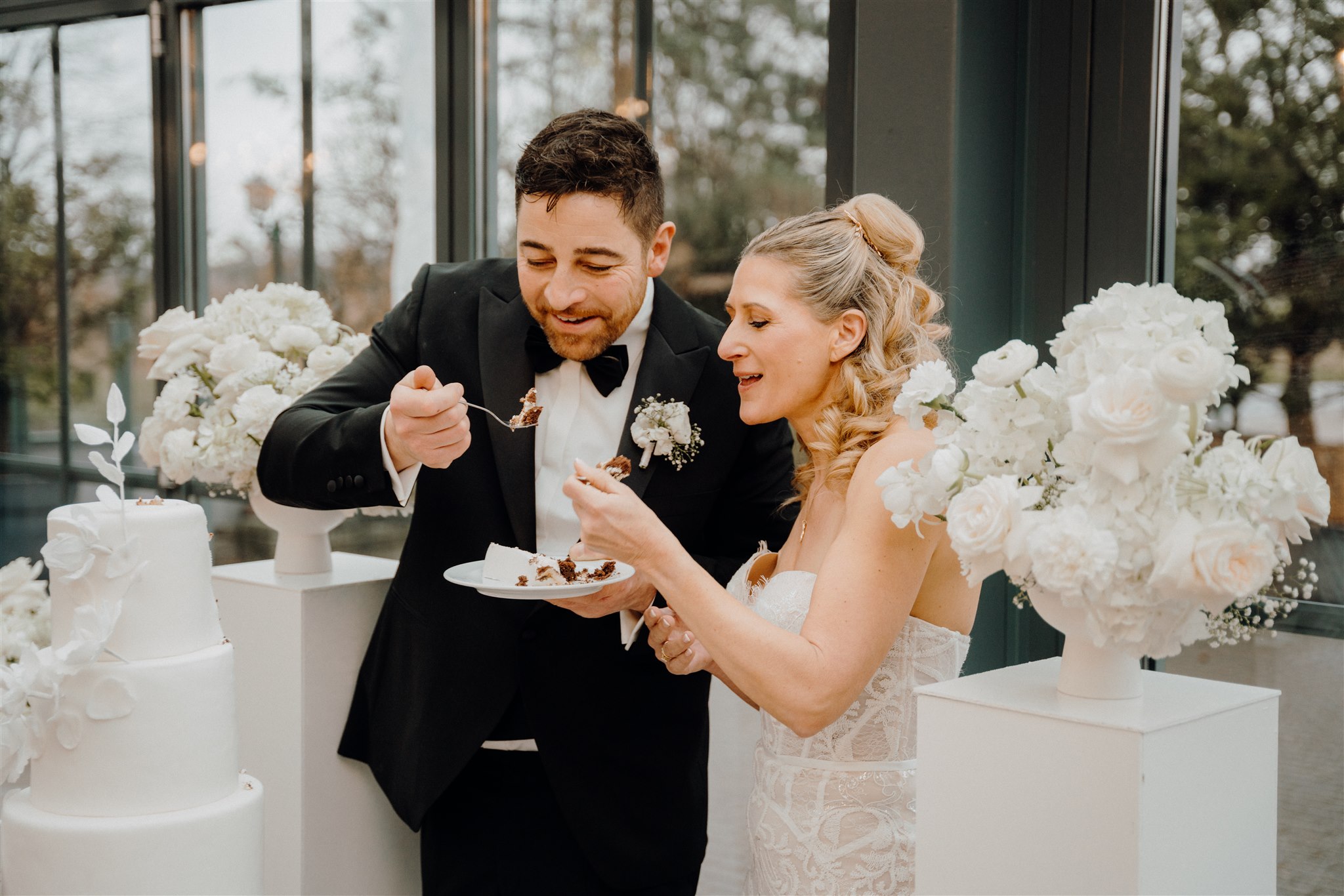 Brautpaar teilt sich ein Stück Hochzeitstorte zwischen Blumensäulen, Planung: Sophia von Aspern, von Aspern Weddings, Lüneburg, Hamburg, Hannover, Bremen