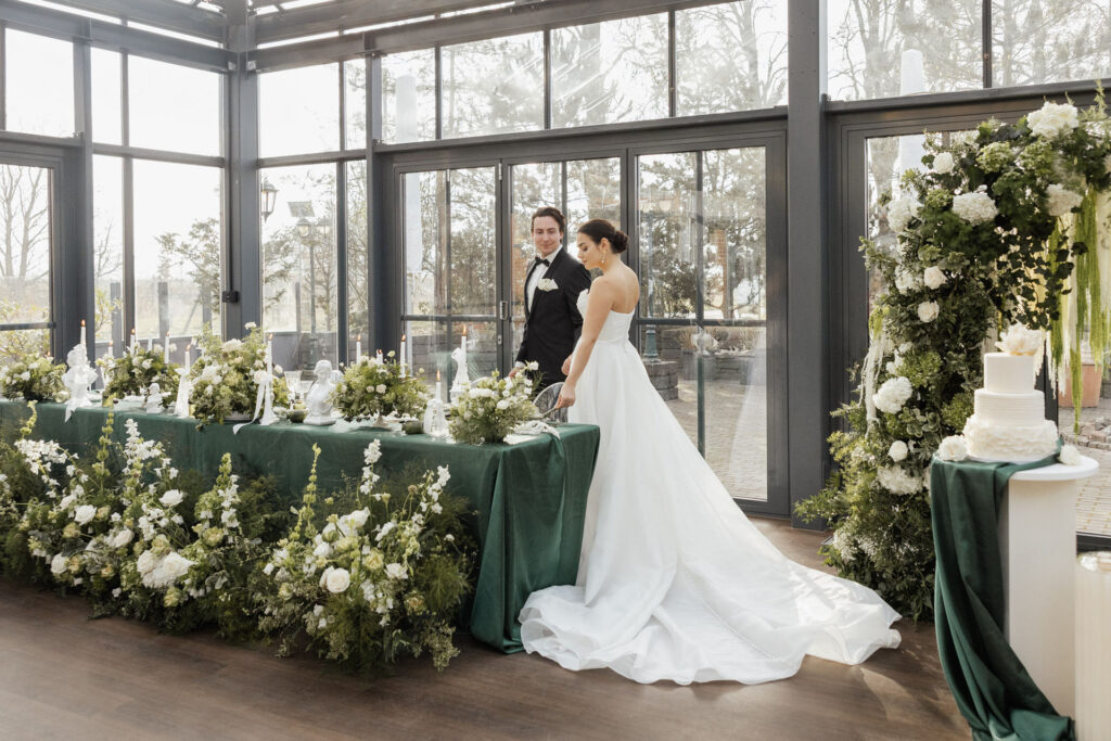 Das Brautpaar spaziert entspannt an der festlich gedeckten Tafel vorbei und wirft einen liebevollen Blick auf das stilvolle Hochzeitskonzept – geplant von von Aspern Weddings.