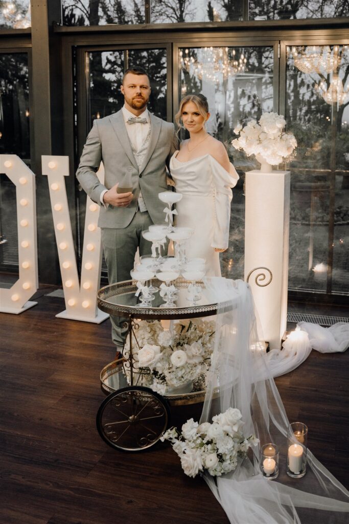 Braut und Bräutigam stehen hinter dem Champagnertower auf dem Teewagen, Planung: Sophia von Aspern, von Aspern Weddings, Lüneburg, Hamburg, Hannover, Bremen