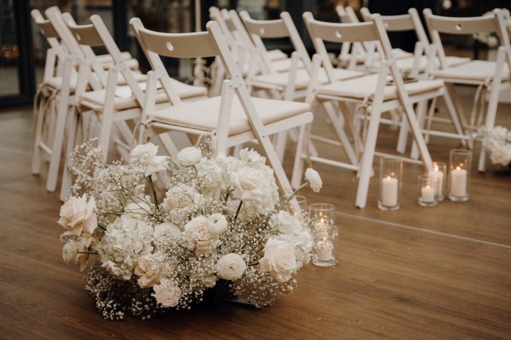 Trauungssetup mit weißen Klappstühlen und Blumengestecken und Kerzen, Planung: Sophia von Aspern, von Aspern Weddings, Lüneburg, Hamburg, Hannover, Bremen
