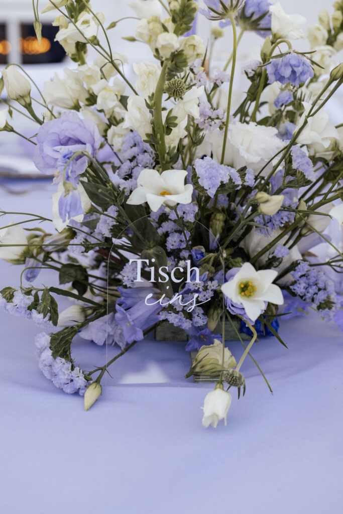 Blumengesteck in Lila und Violett neben eleganter Tischnummer auf dem Hochzeitstisch im Atlantic Hotel Travemünde, exklusive Hochzeitsplanung Sophia von Aspern, von Aspern Weddings, Hamburg, Bremen, Hannover, Niedersachsen.