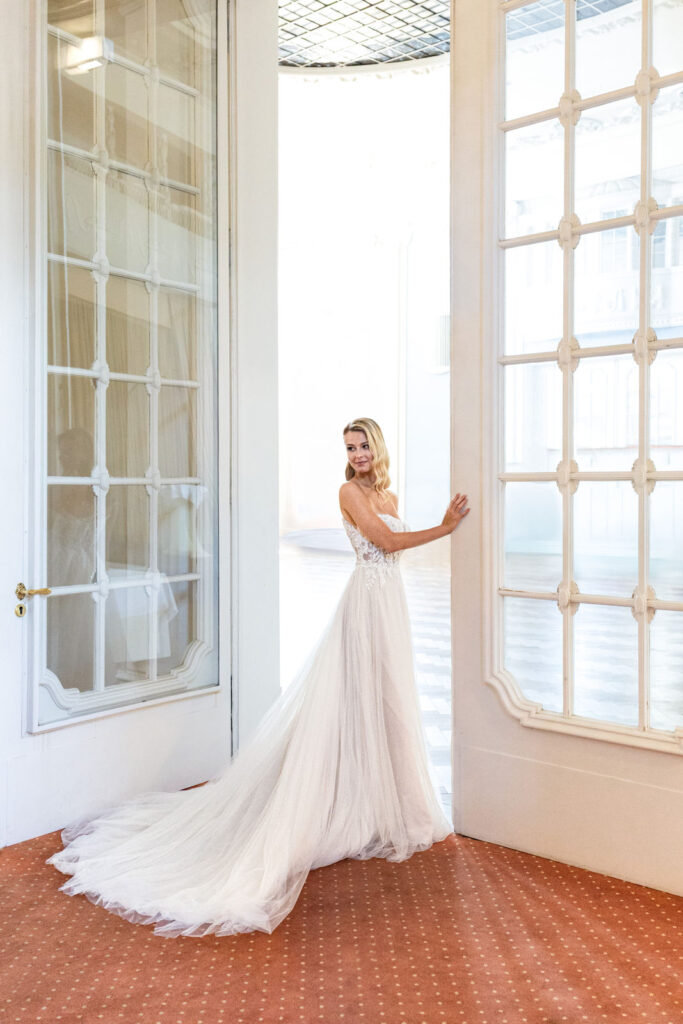 Die Braut steht im Türrahmen des prachtvollen Ballsaals im Atlantic Grand Hotel Travemünde und lässt den Blick in den festlich vorbereiteten Raum schweifen – ein Moment voller Eleganz, eingefangen von Sophia von Aspern, von Aspern Weddings, Hochzeitsplanung in Hamburg, Hannover, Bremen und Niedersachsen