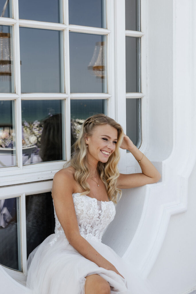 Braut steht am Fenster zum Balkon des Atlantic Hotels Travemünde mit Blick auf die Ostsee, stilvolle Hochzeitsplanung Sophia von Aspern, von Aspern Weddings, Hamburg, Bremen, Hannover, Niedersachsen.