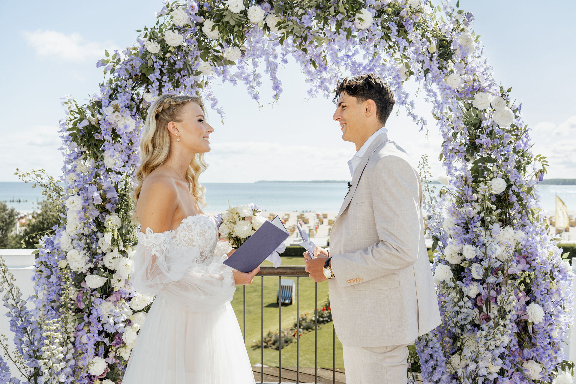 rautpaar gibt sich sein Eheversprechen vor dem festlich geschmückten Traubogen im Atlantic Hotel Travemünde mit Ostsee im Hintergrund, stilvolle Hochzeitsplanung Sophia von Aspern, von Aspern Weddings, Hamburg, Bremen, Hannover, Niedersachsen.