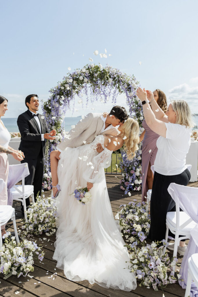 Brautpaar beim Auszug nach der Trauung mit romantischem Dipkiss vor der Ostseekulisse im Atlantic Hotel Travemünde, exklusive Hochzeitsplanung Sophia von Aspern, von Aspern Weddings, Hamburg, Bremen, Hannover, Niedersachsen.
