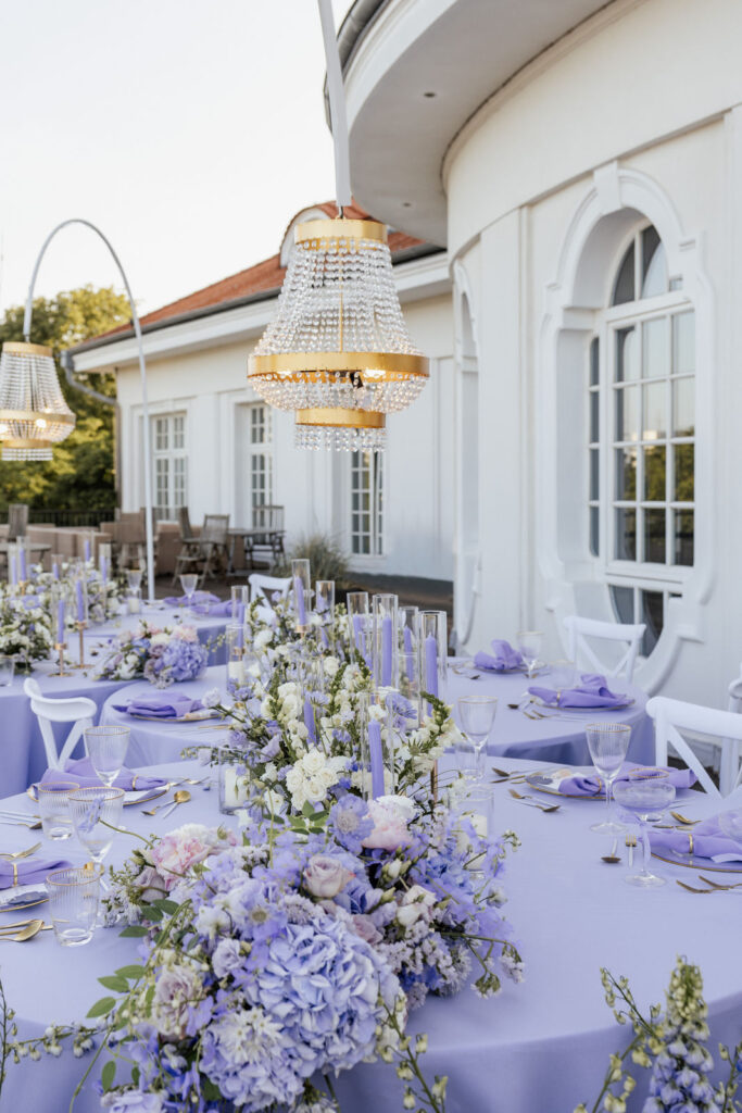 Kronleuchter über den Hochzeitstischen mit violetten Blumengestecken, Hochzeitsplanung Sophia von Aspern, Hamburg, Niedersachsen, Schleswig-Holstein.
