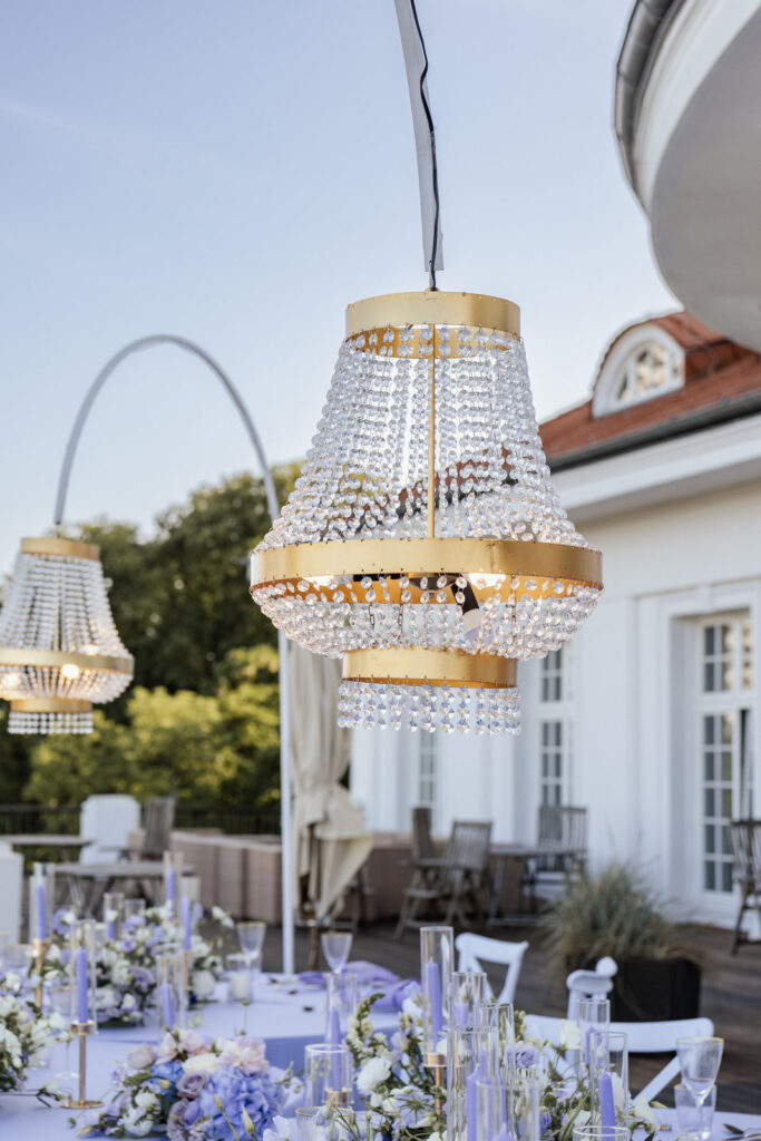 Kronleuchter leuchten über dem festlich gedeckten Hochzeitstisch, im Hintergrund das Atlantic Hotel Travemünde, stilvolle Hochzeitsplanung Sophia von Aspern, von Aspern Weddings, Hamburg, Bremen, Hannover, Niedersachsen.