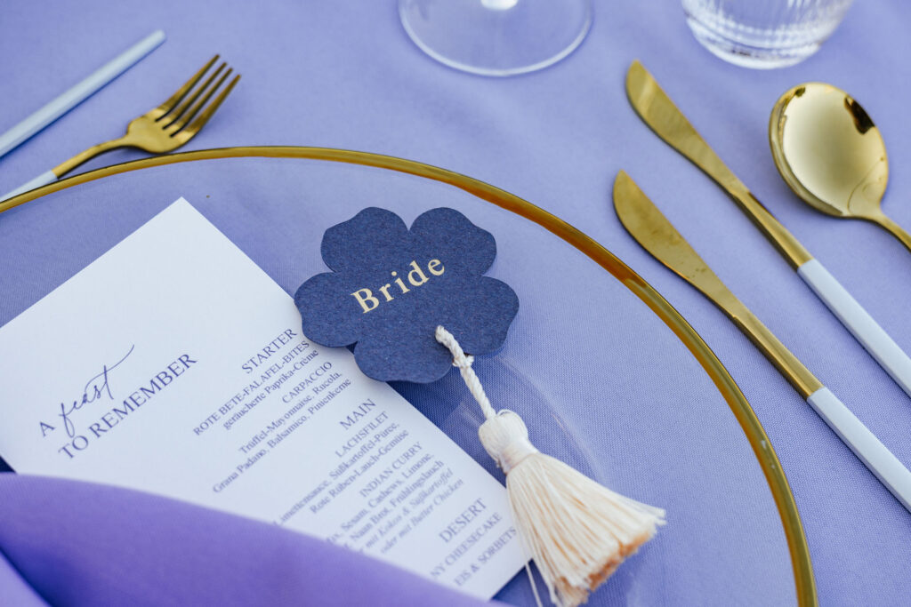 Namensschild mit der Aufschrift „Braut“ liegt neben der Menükarte auf einem festlichen Platzteller, elegantes Tablesetting im Atlantic Hotel Travemünde, Hochzeitsplanung Sophia von Aspern, von Aspern Weddings, Hamburg, Bremen, Hannover, Niedersachsen.