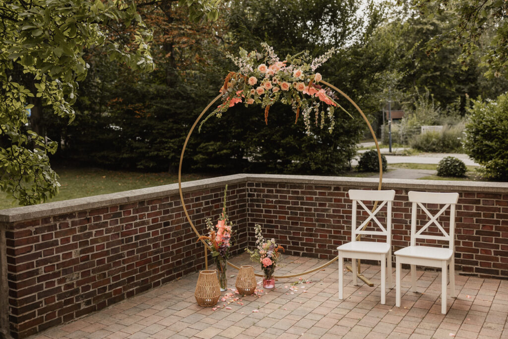 Trauungssetup mit stilvoll arrangierter Dekoration: ein heller, moderner Rahmen mit eleganten Stühlen, sanften Stoffen und floralen Akzenten, die eine warme und intime Atmosphäre schaffen. Die Dekoelemente von Atelier Feingefühl fügen sich harmonisch in das Gesamtbild ein und setzen dezente Highlights für eine emotionale Zeremonie. Stichwörter: Sophia von Aspern, Hochzeitsplanung, von Aspern Weddings, Hamburg, Bremen, Hannover, Niedersachsen.