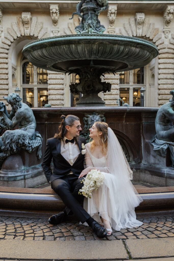 Brautpaar vor dem Hamburger Rathaus am Brunnen, emotionale Standesamt Hochzeit in Hamburg nahe der Elbphilharmonie, stilvolle Hochzeitsplanung mit persönlichem Blick für Details, begleitet von Sophia von Aspern, Hochzeitsplanerin für Hamburg, Hannover, Bremen und Lüneburg, umgesetzt mit von Aspern Weddings.