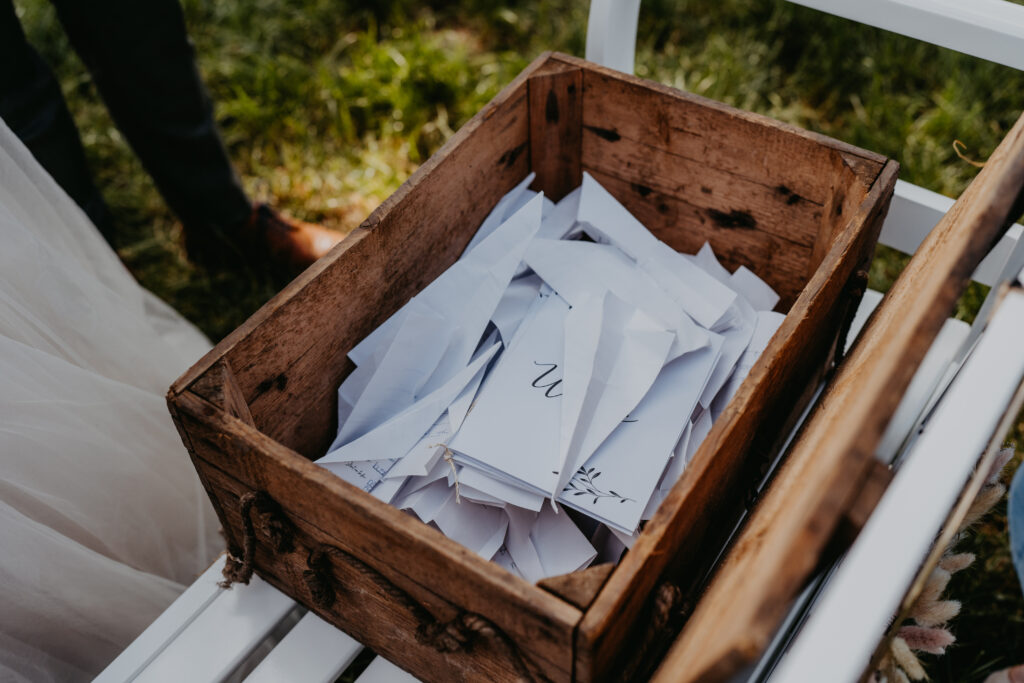 Freie Trauung in Hamburg mit emotionalem Trauritual: Gäste schreiben persönliche Wünsche auf Zettel, die in einer Zeitkapsel gesammelt werden, während das Brautpaar das Hochzeitsritual gemeinsam durchführt. Intimer Moment voller Bedeutung, eingebettet in eine stilvolle Hochzeitsplanung von Sophia von Aspern. Persönliche Zeremonie mit klarer Symbolik, umgesetzt für moderne Hochzeiten in Hamburg, Hannover, Bremen und Niedersachsen, passend zum Anspruch von von Aspern Weddings.