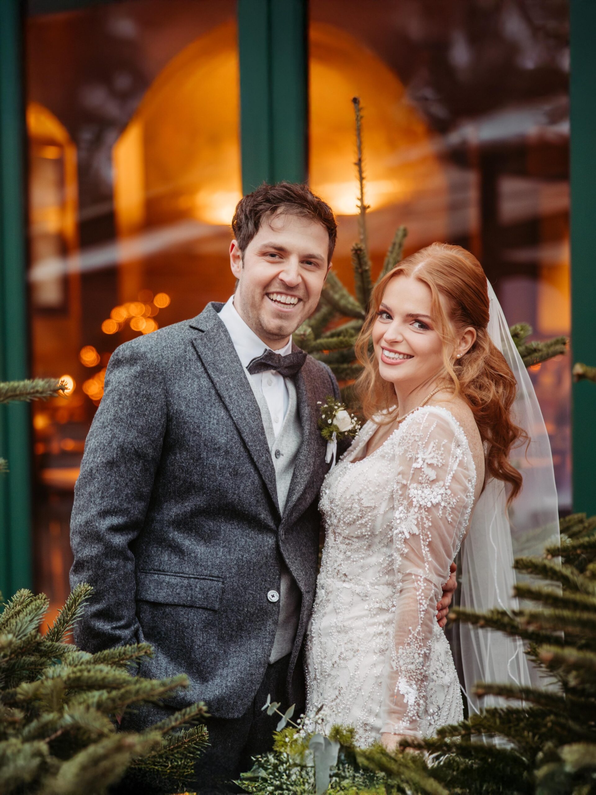 Braut und Bräutigam stehen bei einer Winterhochzeit auf Gut Thansen zwischen Tannenbäumen und genießen einen ruhigen Moment in festlicher Atmosphäre. Professionelle Hochzeitsplanung und Zeremonienmeister Begleitung durch Sophia von Aspern für exklusive Hochzeiten in Hamburg, Bremen, Hannover und Niedersachsen.