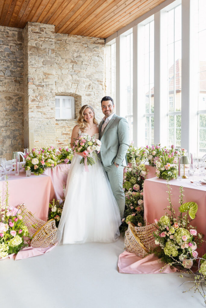 Brautpaar steht vor einem stilvoll gedeckten Tischsetting in Rose und Lime mit moderner, floraler Dekoration und eleganten Details. Exklusive Hochzeitsplanung von Sophia von Aspern für hochwertige Hochzeiten in Hamburg, Bremen, Hannover und Niedersachsen.