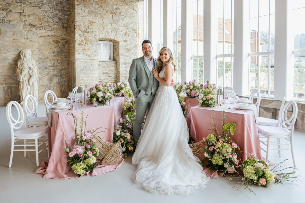 Brautpaar steht vor einem floralen Tischsetting in Rose und Lime in der Orangerie Gut Ostenwalde und wird von moderner, eleganter Hochzeitsdekoration umrahmt. Stilvolle Hochzeitsplanung von Sophia von Aspern für exklusive Hochzeiten in Hamburg, Bremen, Hannover und Niedersachsen.