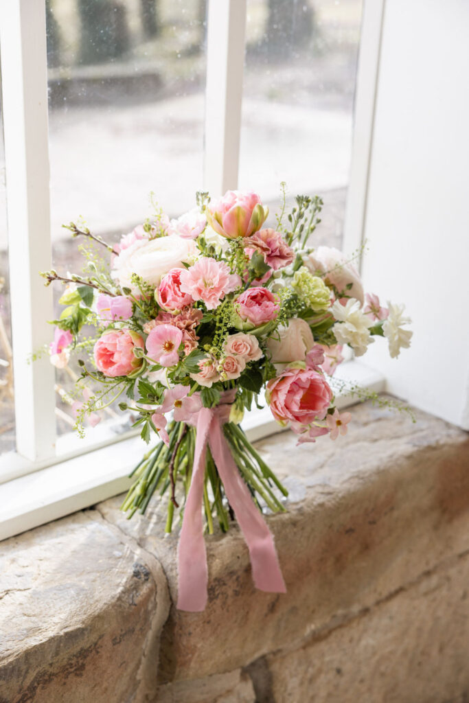 Brautstrauß steht vor einem Fenster, Licht fällt auf die florale Gestaltung in Lime und Rose mit frischen Grüntönen und zarten Roséakzenten, stilvolle Hochzeitsplanung in Hamburg, Bremen und Hannover von Sophia von Aspern von Aspern Weddings