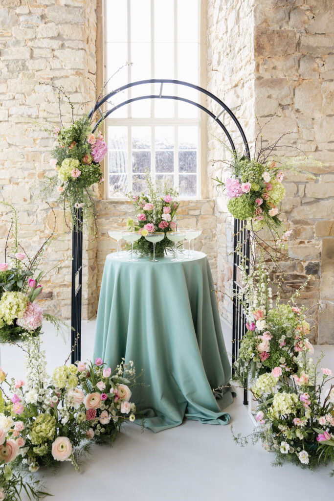 Champagnerturm Hochzeit aufgebaut auf einem Tisch mit grüner Tischdecke unter einem Traubogen, modernes Trauung Setup und stilvolle Hochzeitsdeko bei freier Trauung in Niedersachsen, Hamburg, Bremen und Hannover Hochzeitsplanung von Aspern Weddings Sophia von Aspern
