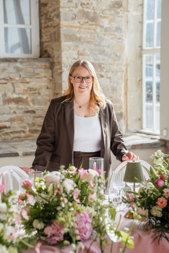 Sophia von Aspern steht hinter einem aufwendig gestalteten floralen Tischsetting mit modernen Blumenarrangements und eleganten Details. Hochwertige Hochzeitsplanung von von Aspern Weddings für exklusive Hochzeiten in Hamburg, Bremen, Hannover und Niedersachsen.
