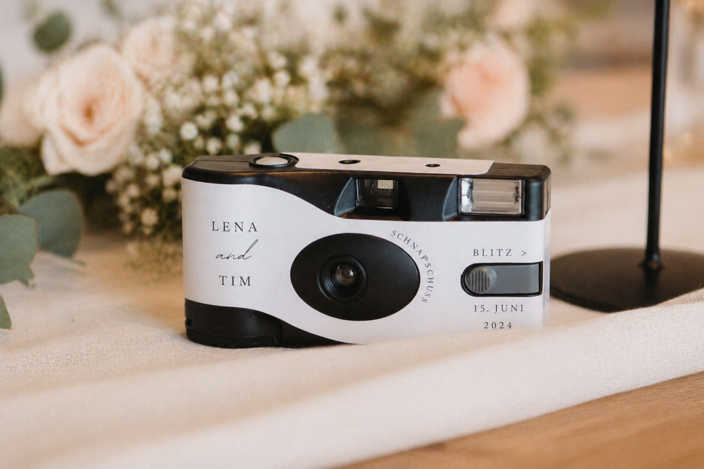 Einwegkamera liegt dekorativ auf einem Hochzeitstisch zwischen stilvoller Papeterie und floralen Details, moderner und eleganter Look mit warmem Licht, Hochzeitsplanung von Aspern Weddings in Hannover, Niedersachsen, inspiriert von hochwertigen Hochzeiten in Hamburg und Bremen mit viel Liebe zum Detail