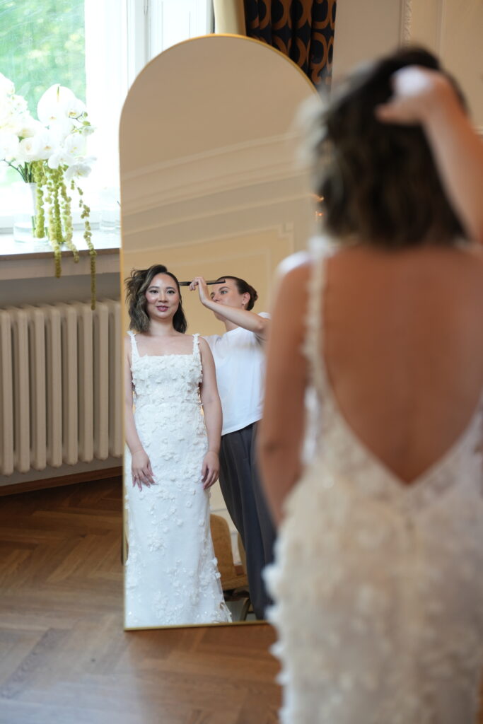 Braut beim Getting Ready im Schloss Ovelgönne, während Stylistin Marta den Schleier einsteckt und die Braut in den Spiegel schaut. Begleitet von Sophia von Aspern als Zeremonienmeisterin von von Aspern Weddings. Hochzeitsplanung in Hamburg, Bremen, Hannover und Niedersachsen.