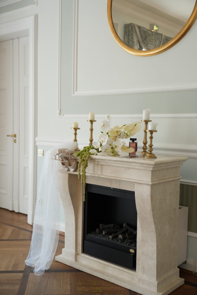 Stilvoller Kamin im Schloss Ovelgönne mit Brautschleier und Brautstrauß als elegantes Detail einer Hochzeit, begleitet von Sophia von Aspern als Zeremonienmeisterin von von Aspern Weddings. Hochzeitsplanung in Niedersachsen, Hamburg, Bremen und Hannover.