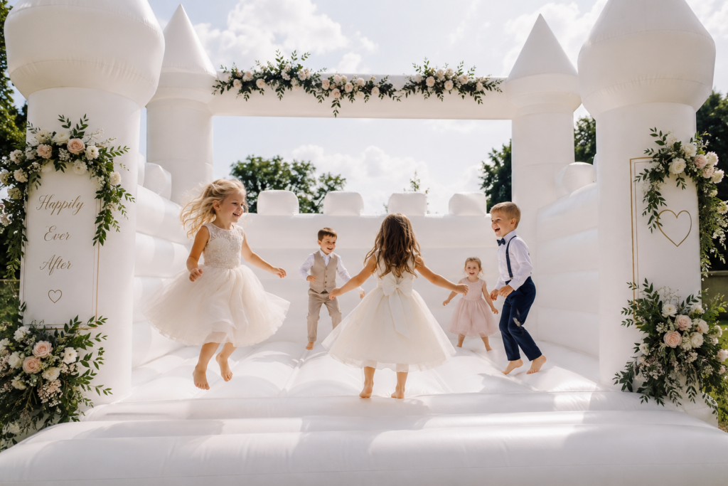 Kinder spielen ausgelassen auf einer weißen Hüpfburg bei einer Hochzeit und haben sichtbar Spaß während der Feier. Eine Hüpfburg kann bei der Hochzeitsplanung in Hamburg, Bremen, Hannover und Niedersachsen eine tolle Ergänzung für Familien mit Kindern sein.