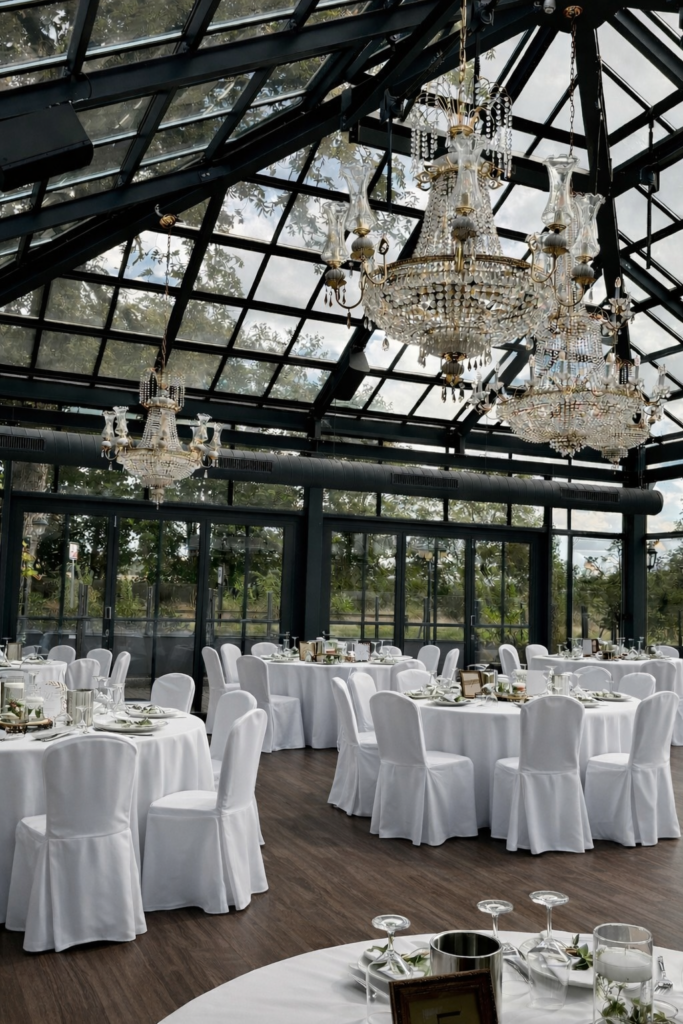 Elegantes Tischsetting in der Hochzeitslocation Glashütte in Adendorf mit bodenlangen Tischdecken, floraler Dekoration und Stühlen mit weißen Stuhlhussen. Stilvolle Hochzeitsdekoration und Hochzeitsplanung in Hamburg, Bremen, Hannover und Niedersachsen von Sophia von Aspern.