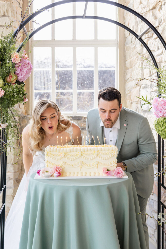 Brautpaar pustet gemeinsam die Kerzen einer modernen rechteckigen Hochzeitstorte in der Orangerie Gut Ostenwalde aus. Elegantes florales Hochzeitssetting mit exklusiver Hochzeitsplanung von Aspern Weddings für stilvolle Hochzeiten in Hamburg, Bremen, Hannover und Niedersachsen.