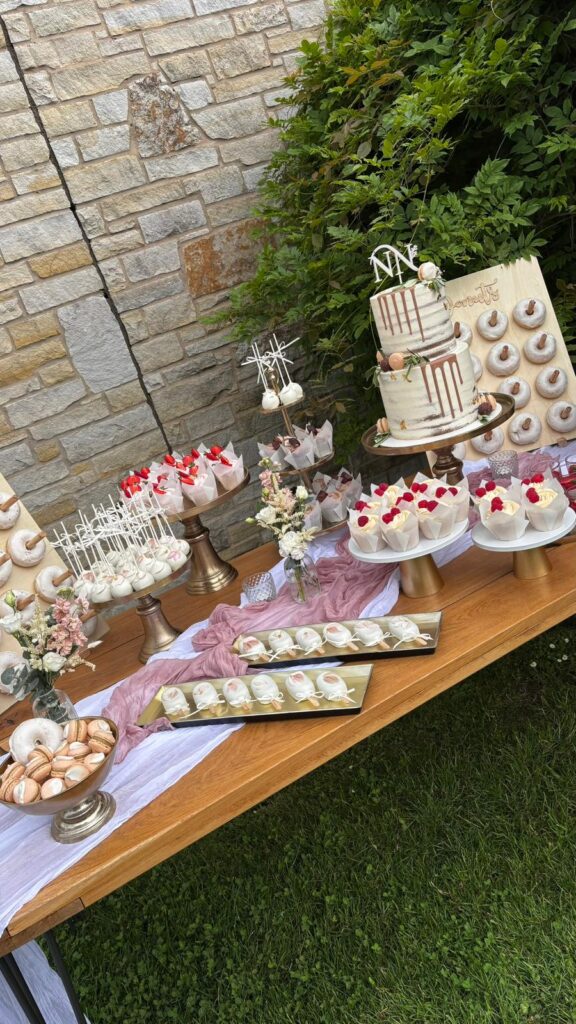 Opulenter Sweet Table im Rittergut Remmeringhausen mit zweistöckiger Hochzeitstorte, Donuts, Dessertgläsern, Cupcakes, Macarons, Cakepops und Cakecicles in einem stimmigen Farbkonzept. Exklusive Hochzeitsplanung von Aspern Weddings für stilvolle Hochzeiten in Hamburg, Bremen, Hannover und Niedersachsen, umgesetzt mit Sanelas Tortenwelt.