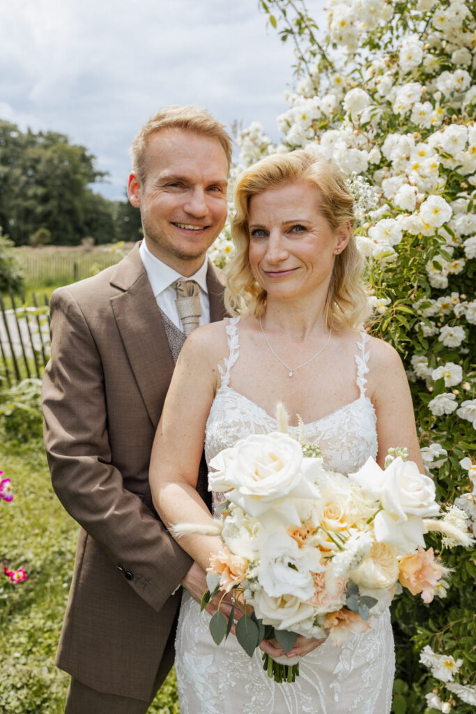 Brautpaar bei einem Paarshooting vor einem blühenden Rosenstrauch im Rittergut Remeringhausen. Die historische Hochzeitslocation in Niedersachsen bietet zahlreiche malerische Fotokulissen. Hochzeitsplanung von Sophia von Aspern, von Aspern Weddings, in Hamburg, Hannover, Bremen und Niedersachsen.