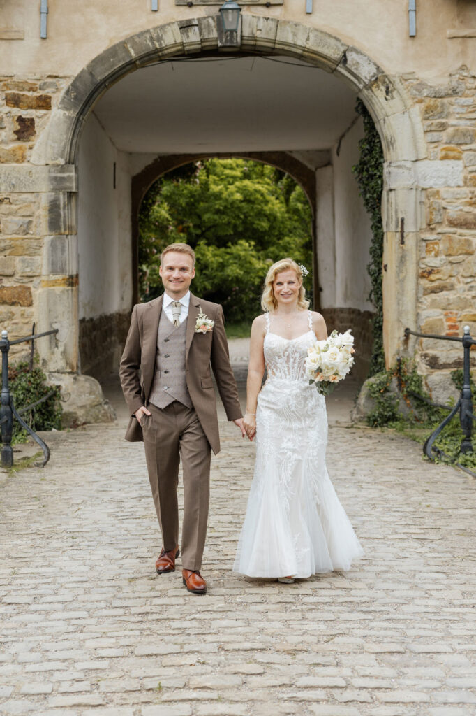 Brautpaar vor dem Torhaus des Ritterguts Remeringhausen während eines Paarshootings. Die historische Architektur der Hochzeitslocation nahe Hannover schafft eine elegante Kulisse für Hochzeitsbilder. Hochzeitsplanung von Sophia von Aspern, von Aspern Weddings, in Hamburg, Hannover, Bremen und Niedersachsen. Foto: Sarah Prahm.